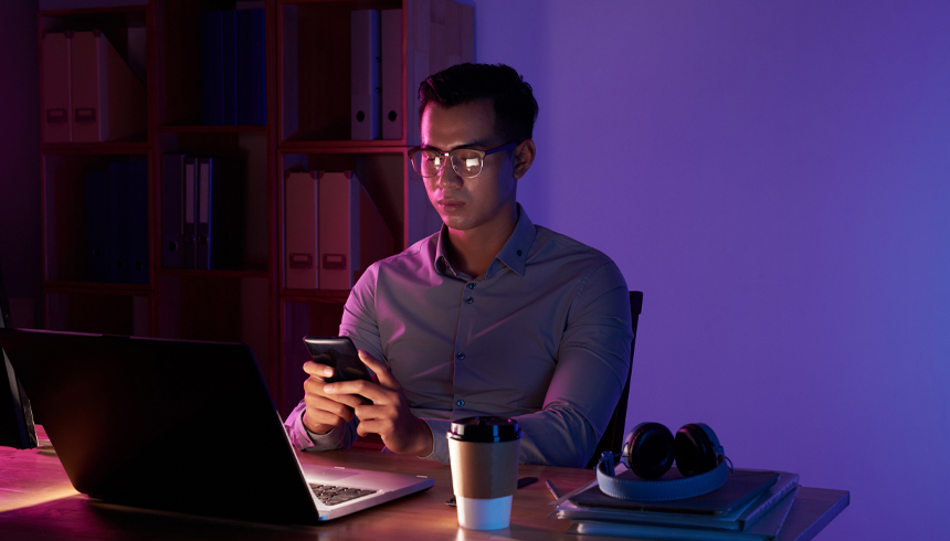 Asian man seated infront of laptop texting